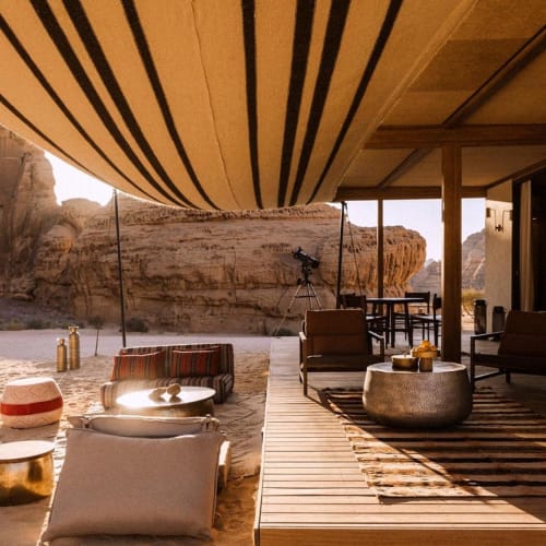 Eine Outdoor-Lounge mit modernen Möbeln und einem gestreiften Sonnensegel mit Blick auf felsiges Wüsten Gelände.
