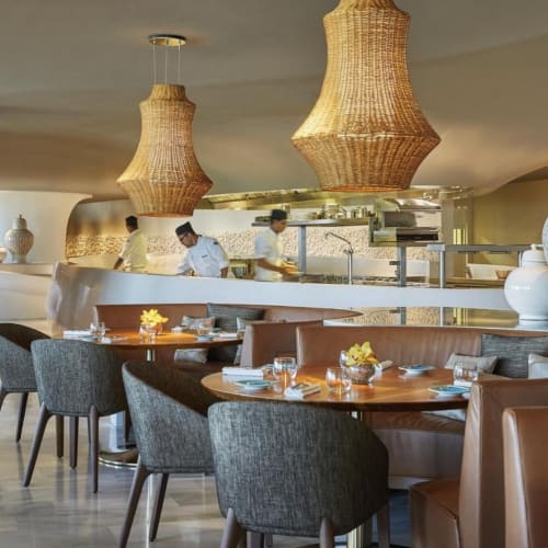 Elegantes Restaurant-Innenraum mit modernem und rustikalem Dekor, mit geflochtenen Hängeleuchten, großen weißen Tonvasen und ordentlich gedeckten Tischen.