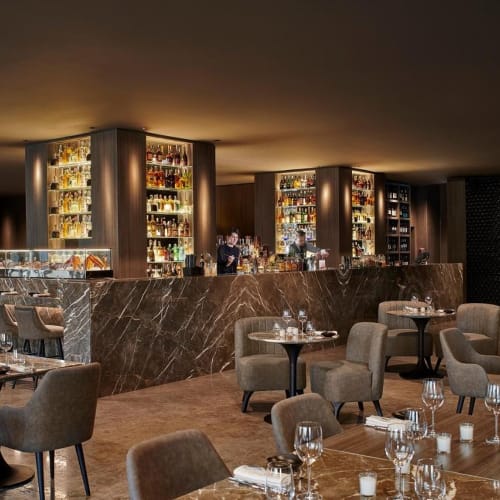 Elegant restaurant interior with a well-stocked bar, comfortable seating, and neatly set tables on wood flooring.