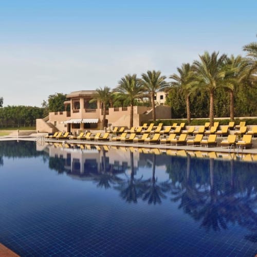 A large outdoor swimming pool at the Marriott Mena House Cairo with yellow lounge chairs and palm trees along the poolside.