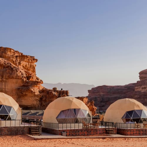Luxury dome tents set up in the Wadi Rum desert with towering red rock formations in the background.
