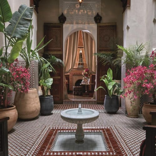 Elegant Moroccan courtyard with lush plants and a central Fountain in a luxurious riad setting.