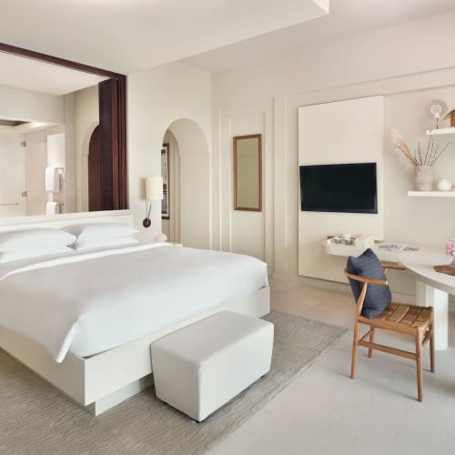Ein modernes, elegantes Hotelzimmer mit einem großen Bett, weißer Einrichtung und einem kleinen Essbereich mit zwei Stühlen und einem Tisch.