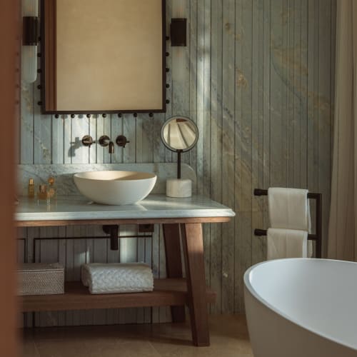 A modern bathroom with a marble countertop, a vessel sink, and a large mirror above it. The room features rustic wooden accents and a freestanding bathtub.