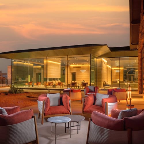 Elegant outdoor seating area with plush chairs and a modern glass building reflecting a sunset sky.