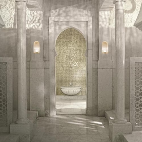 An elegant, white marble interior of a Hammam with columns and intricate details, illuminated softly by wall lamps.