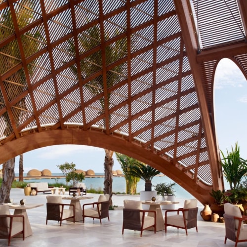 Luxus-Lounge-Bereich mit modernen Möbeln und Topfpflanzen unter einer Holzarchitektur, Blick auf das Meer.