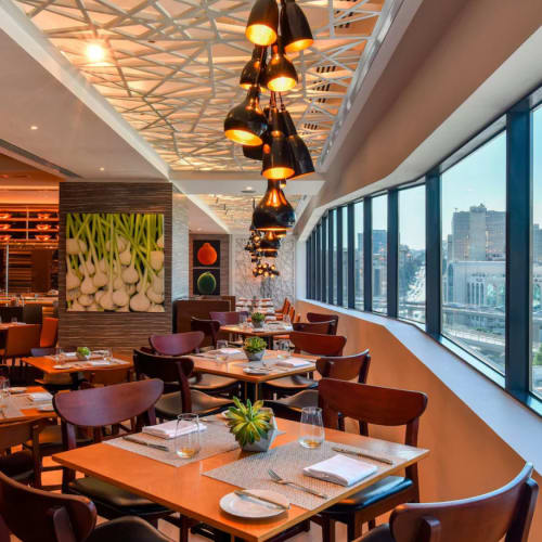 Elegantes Restaurantinterieur mit Holztischen, moderner Pendelleuchte und großem Fenster mit Stadtblick.