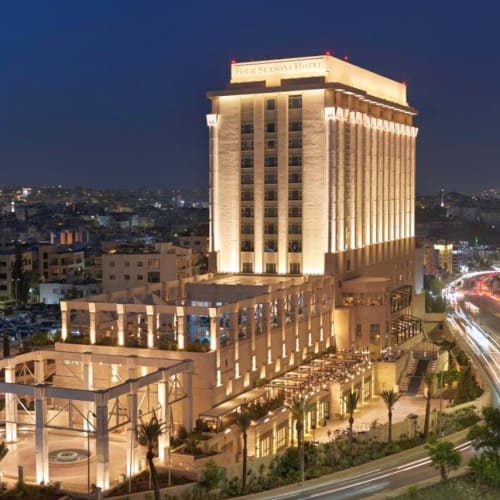 Ein hohes beleuchtetes Four Seasons Hotel Gebäude steht bei Nacht in einer Stadtlandschaft, mit belebten Straßen und Stadtlichtern umgeben.