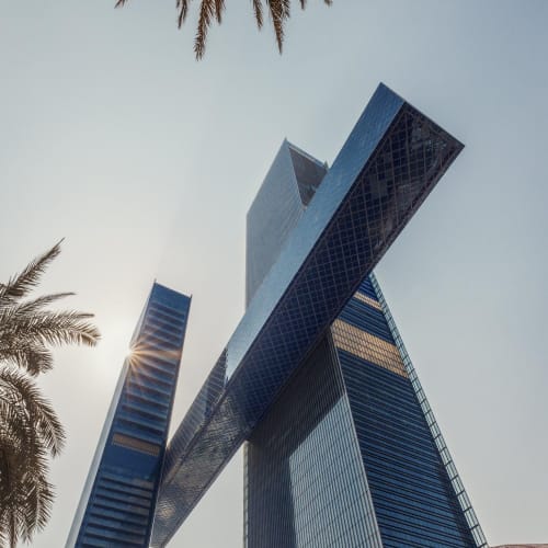 A modern skyscraper with a distinctive cantilevered section, set against a clear sky with palm trees in the foreground.