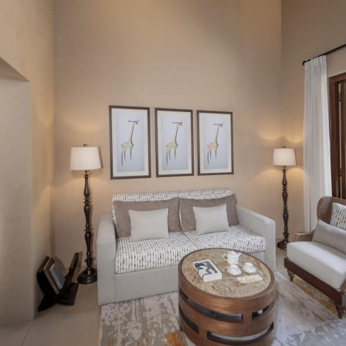 Gemütliches Wohnzimmer in einer Villa mit Sofa, Sessel, Couchtisch, Wandbildern mit Giraffenmotiv und Stehlampen, mit einer Schiebetür, die zu einem Außenpoolbereich führt.