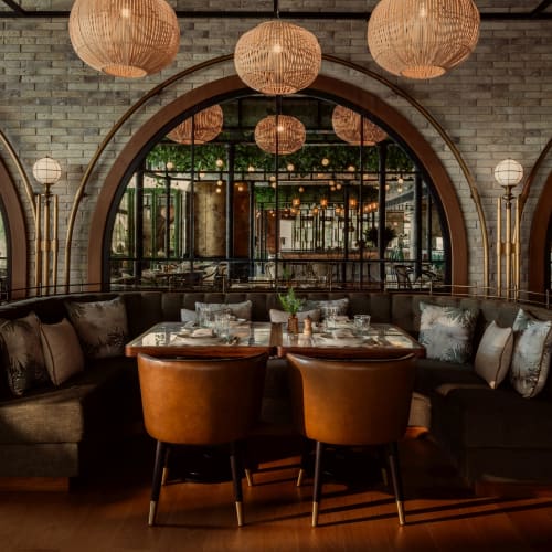 Eine gemütliche Restaurant-Ecke mit einer gebogenen Bank, zwei Stühlen und hängenden Papierlaternen in einer warm beleuchteten Umgebung.