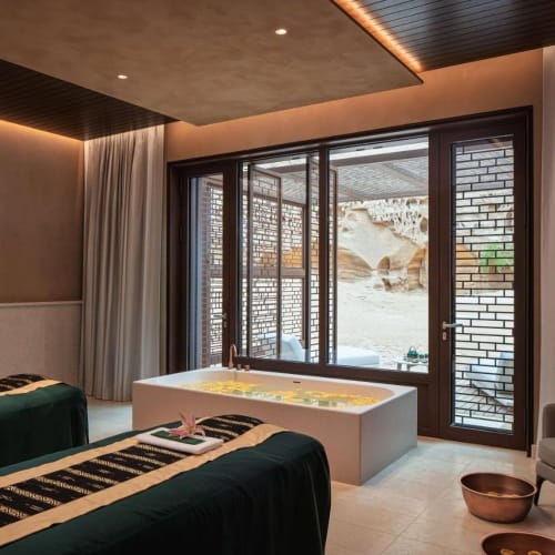 Luxuriöser Spa-Raum mit zwei Massagebetten, einer Badewanne vor großen Fenstern und Blick auf die Felsen draußen.
