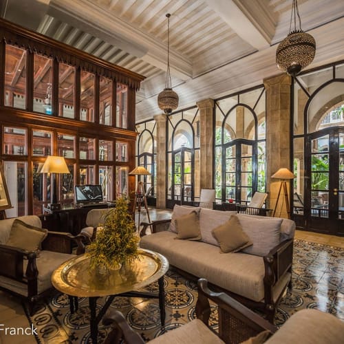Luxuslobby eines Hotels mit antiken Möbeln, großen bogenförmigen Fenstern und dekorativen Hängeleuchten.