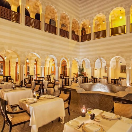 Elegant restaurant interior with white-clothed tables, black chairs, and ambient lighting in a spacious, two-story setting.