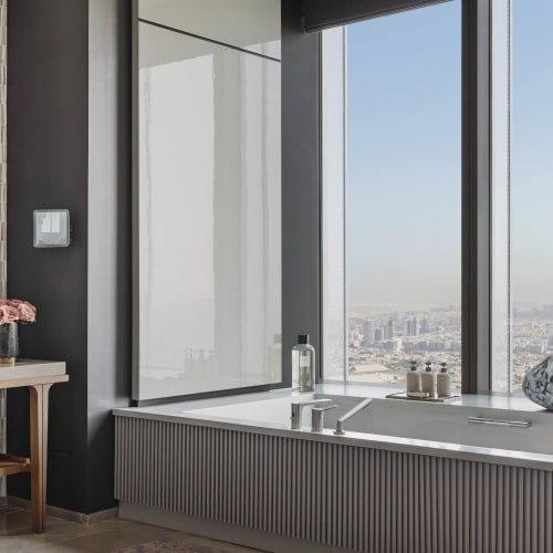 Ein luxuriöses Badezimmer mit einem großen Fenster, das eine Stadtansicht bietet, mit Badewanne und dekorativen Gegenständen sowie einem eleganten Waschtisch.
