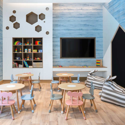 Buntes Spielzimmer für Kinder mit kleinen Tischen und Stühlen, einem wandmontierten Bildschirm und verspielter Dekoration in einem modernen, hellen Raum.