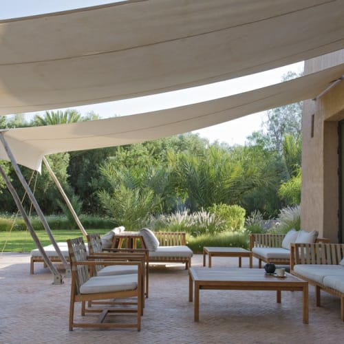 Outdoor terrace with wooden furniture and large fabric shades overhead, surrounded by greenery.