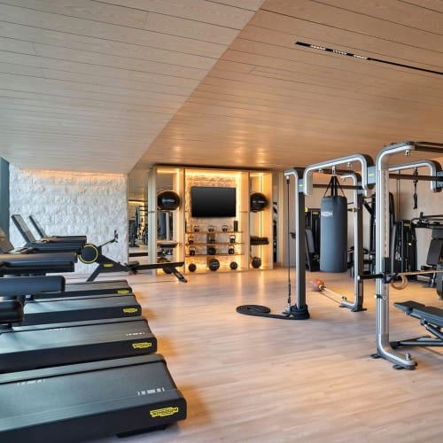 Modernes Fitnessstudio mit Laufbändern, Kraftmaschinen und einem großen Fernseher in einem gut beleuchteten Raum mit Holzboden.