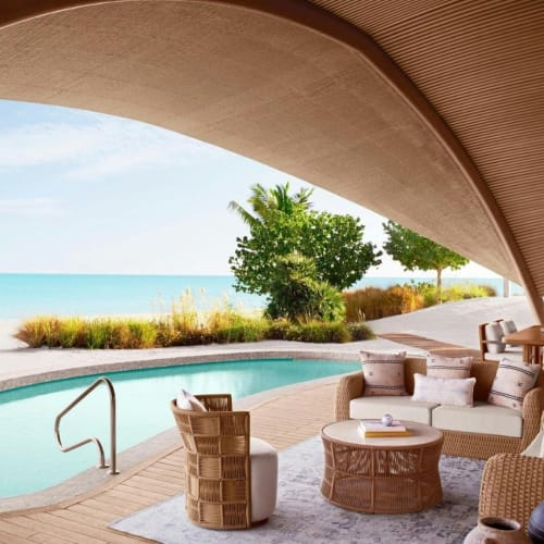 Luxus-Pool-Villa mit Blick auf den Strand und den Ozean, Sitzbereich im Freien mit Möbeln unter einem gewölbten Dach.