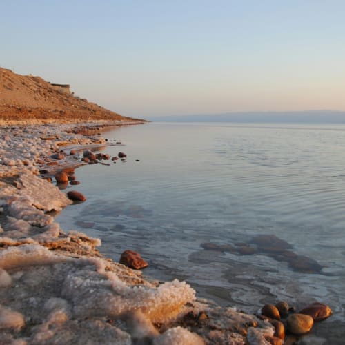 Die Küste des Toten Meeres bei Sonnenuntergang mit Salzformationen und glatten Steinen am Ufer.