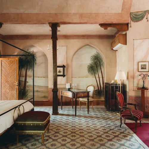 Luxuriöse Hotellsuite mit klassischer Dekoration, Himmelbett, antike Möbel, Topfpflanzen und gefliester Boden.