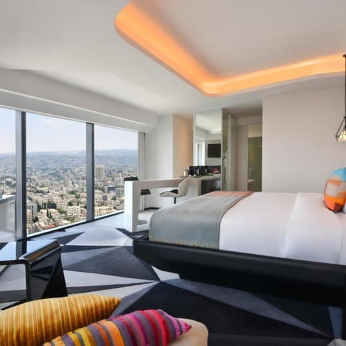Modernes Hotelzimmer mit großem Fensterblick auf die Stadt, einem Kingsize-Bett und zeitgemäßer Einrichtung.