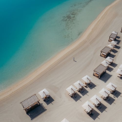 Luftaufnahme eines Strandes mit Sonnenschirmen und Cabanas am türkisfarbenen Wasser.