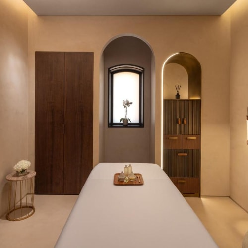 A serene spa treatment room with a white massage bed, minimalist decor, and soft lighting.