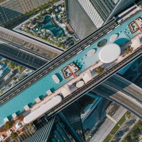 Luftaufnahme eines futuristischen Wolkenkratzers mit Dachpool und Aussichtplattformen in einer modernen Stadt.