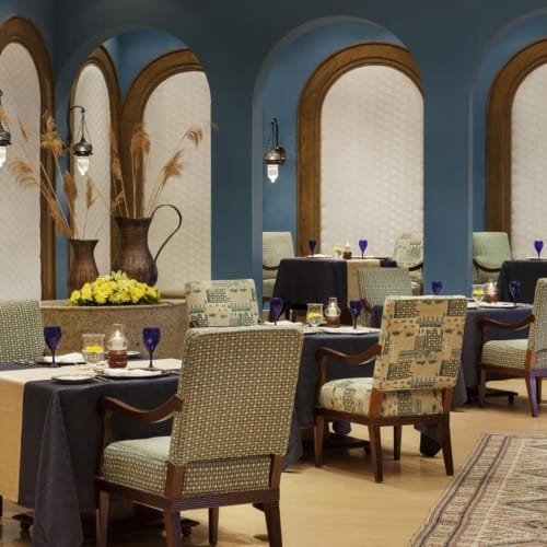 Eleganter Speisesaal mit blauen Wänden, Bögen und dekorierten Tischen mit schwarzen Tischtüchern und blauen Gläsern.