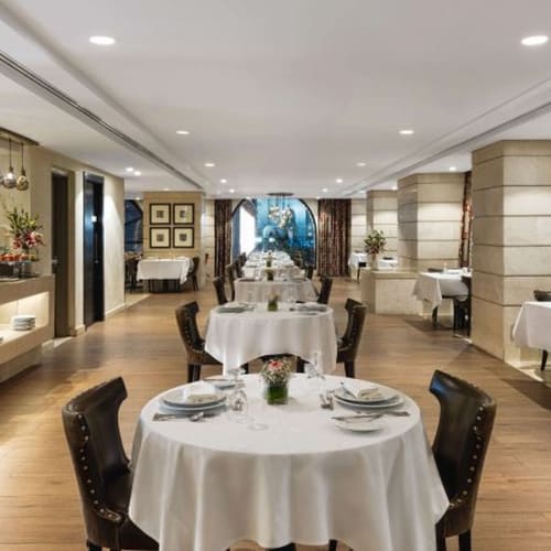Eleganter Speiseraum in einem Hotelrestaurant mit runden Tischen, bedeckt mit weißen Tischdecken, zum Essen gedeckt, und Dekorationselementen an den Wänden.