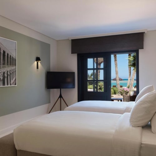 A hotel room with two single beds facing a window overlooking palm trees and the sea in El Gouna.