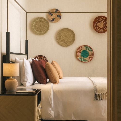 Ein gemütliches Schlafzimmer mit einem ordentlich gemachten Bett, Dekokissen und geflochtenen Wandkörben im minimalistischen Stil.
