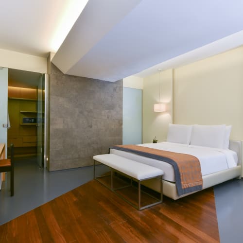 Luxurious hotel room with a white bed, bench, nightstand, and modern decor facing the Dead Sea.