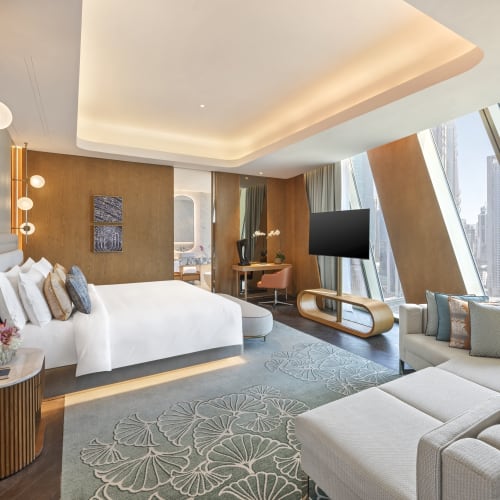 Luxurious hotel room with a large bed, modern decor, and a city view from angled windows in Dubai.