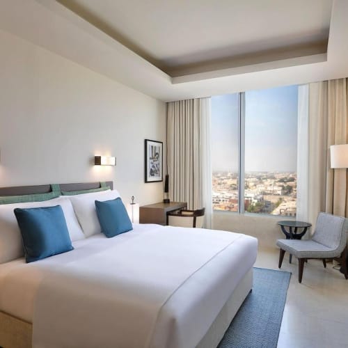 Luxury hotel room with a large bed, blue pillows, a window with city view, and modern furnishings.