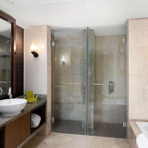 Luxuriöses Hotelbad mit einer Glastür-Dusche, einer Badewanne mit Duschkopf und einer Waschtisch mit Spiegel.
