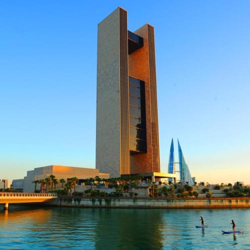 Luftaufnahme des Four Seasons Hotels am Bahrain Bay mit zwei Paddelboardern auf dem Wasser, hohe moderne Wolkenkratzer im Hintergrund und einem klaren blauen Himmel.