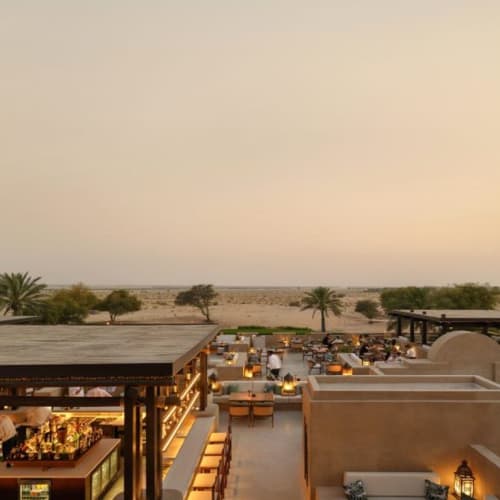 A view of a desert resort during sunset with palm trees and outdoor seating areas.