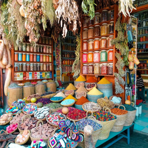 Colorful spice stall in Marrakech Medina's souk with hanging dried herbs and jars of spices.