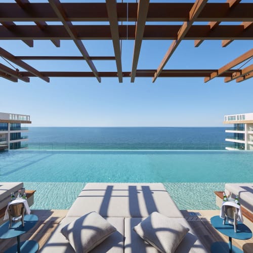 Schwimmbecken mit Liegen und Kissen, das auf den Ozean bei einem Luxushotel blickt.