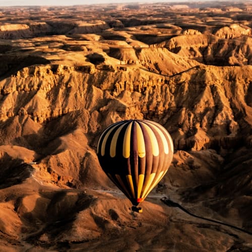 Ein bunter Heißluftballon fliegt über das raue Terrain der ägyptischen Wüste bei Sonnenuntergang.