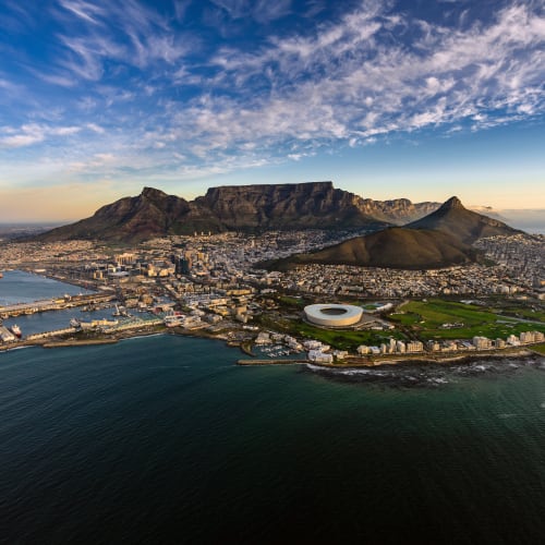 Aerial view of Cape Town showing the city, Table Mountain, and the surrounding coastline during sunset.