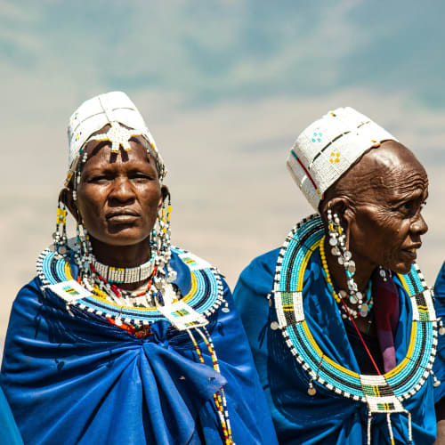 Two Maasai women dressed in traditional blue attire and elaborate bead jewelry in Karatu, Tanzania.