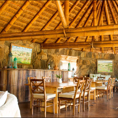 An elegant lounge area with a thatched roof, wooden furniture, and large windows showing scenic views.