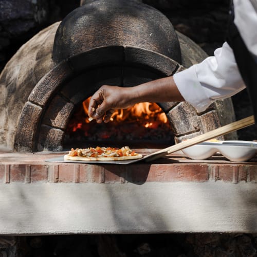 Eine Person belegt eine pizza vor einem holzofen.