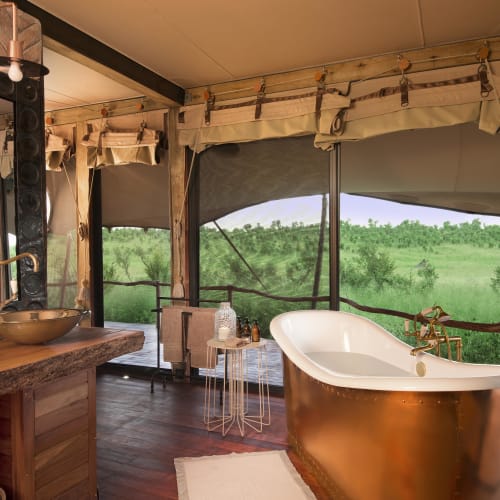 Ein luxuriöses Badezimmer mit freistehender Badewanne mit Blick auf die grüne Landschaft durch große Fenster.