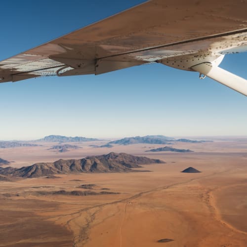 Aerial view of a vast desert landscape with mountain ranges in the distance seen from an airplane window.