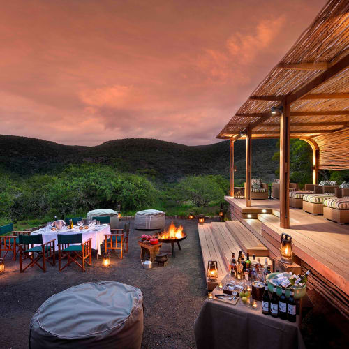 Luxurious outdoor dining area and lounge on a terrace at sunset in a game reserve.